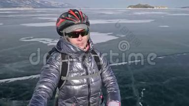女人在冰上骑着自行车走着。 女孩穿着银色的羽绒服，背包和头盔。 冰冰